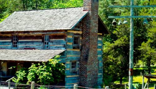 Clinton-Museum Historic log cabin with a stone chimney at the Clinton Museum in Tennessee, surrounded by greenery and wooden fencing.