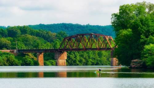 Oak-Ridge-Bridge Old railroad bridge spanning a calm river surrounded by lush green trees and hills