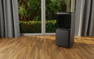 Portable black air conditioner unit on a wooden floor inside a room with large windows and curtains